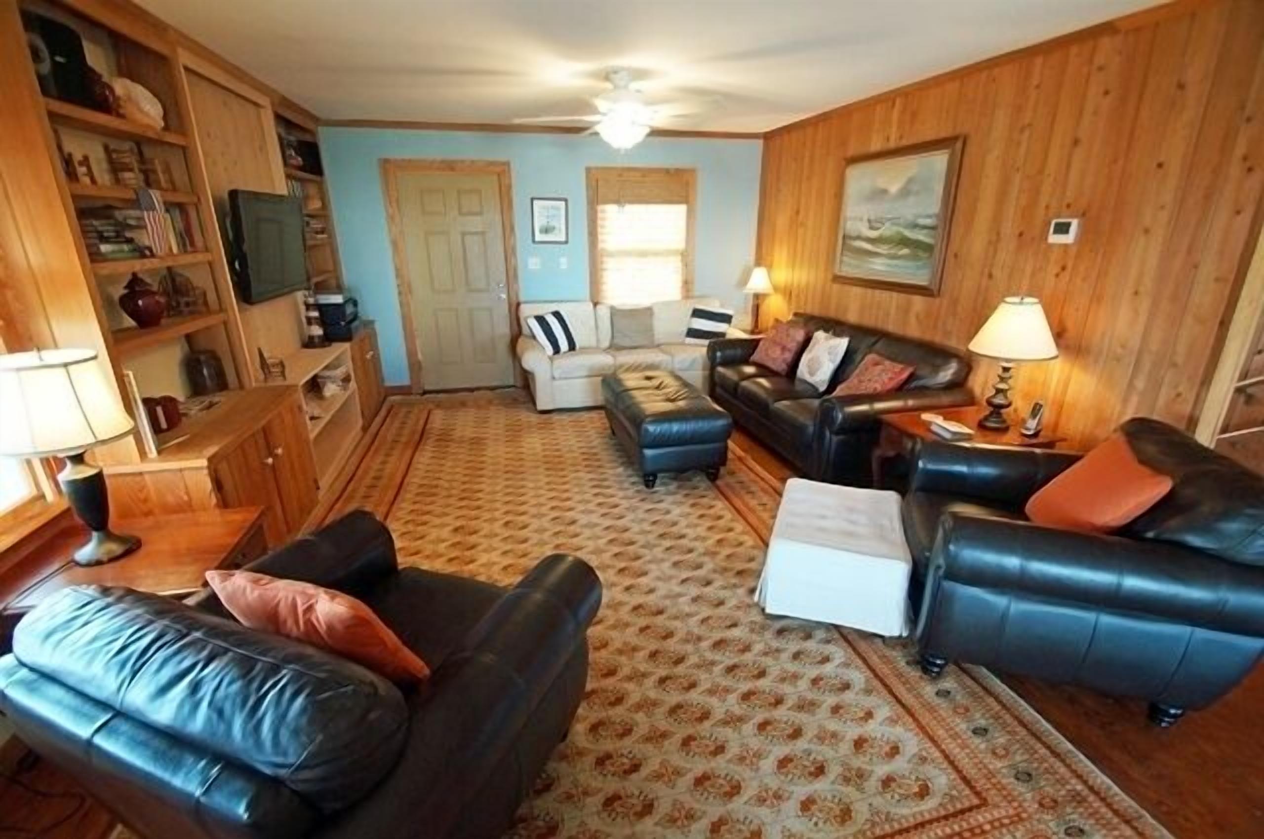 A cozy living room with a fireplace, leather sofas, a coffee table, and a bookshelf.