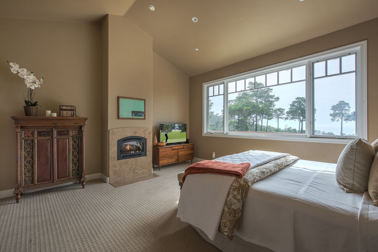 A bedroom with a large window, a fireplace, a television, and a wooden cabinet.