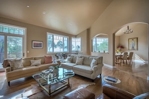 A spacious living room with a large sofa, a glass coffee table, and a dining area with a table and chairs. - 3707 Pacific's Edge Sanctuary ~ Ocean View Estate (Carmel)