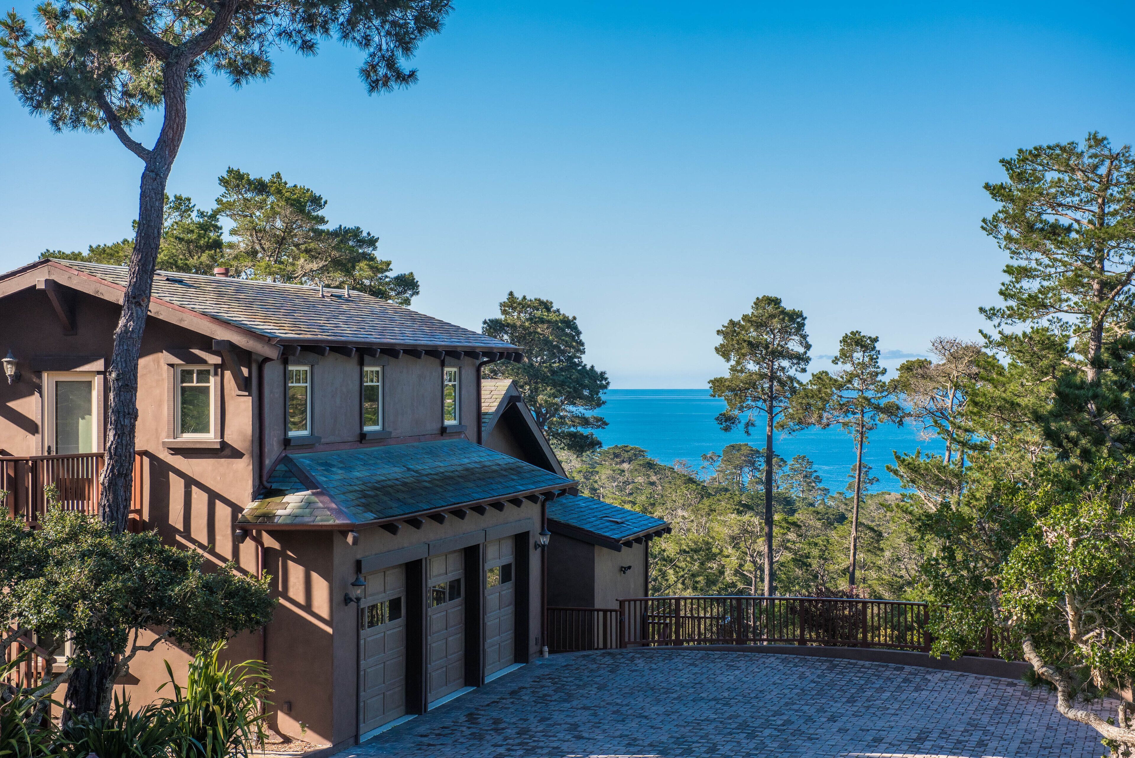 Une maison à deux étages avec un garage, une allée pavée de pierres et une vue sur l’océan.