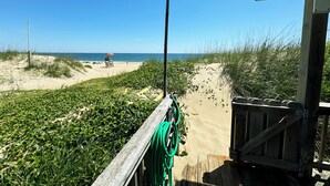 Vista a la playa con una terraza de madera, un banco y una manguera verde.