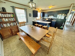A kitchen with a wooden table, chairs, a bookshelf, and a window with blinds. - KD2709- Oceanfront-3 BRs (One Master), Dog Friendly, Outstanding Ocean Views! (Kill Devil Hills)