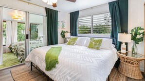 Un dormitorio con cama, ventilador de techo, ventana con cortinas y vista a zonas verdes.