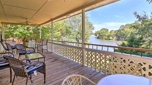 Terraza exterior techada con muebles de mimbre, una mesa y vistas a un río y árboles.