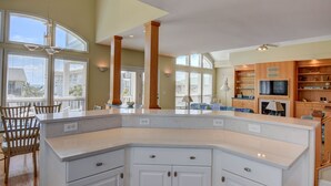 A spacious kitchen with a large island, wooden cabinets, and a dining area with chairs. - Schmid – Very spacious & elegant home with outstanding ocean and sound views (Wrightsville Beach)