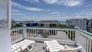 A balcony with white railings and two white lounge chairs. In the background, there are several houses with a view of the ocean. - Schmid – Very spacious & elegant home with outstanding ocean and sound views (Wrightsville Beach)