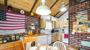 A kitchen with wooden cabinets, a brick wall, and a hanging American flag. - Hunter Hideaway w/ Yard & Deck: 3 Mi to Ski Slopes (Hunter)