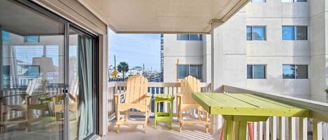 A balcony with a glass door, wooden chairs, a small table, and a white railing.