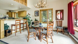 A dining area with a glass table surrounded by wooden chairs, a chandelier, and a view of the outdoors through large windows. - 'Marble Hideaway' Cabin w/ Mountain Views + Deck! (Marble)