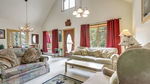 A spacious living room with a high ceiling, a chandelier, and a large window with red curtains. - 'Marble Hideaway' Cabin w/ Mountain Views + Deck! (Marble)