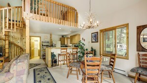 A spacious living area with a high ceiling, a dining table surrounded by chairs, a staircase leading to an upper level, and a view of the outdoors through large windows. - 'Marble Hideaway' Cabin w/ Mountain Views + Deck! (Marble)