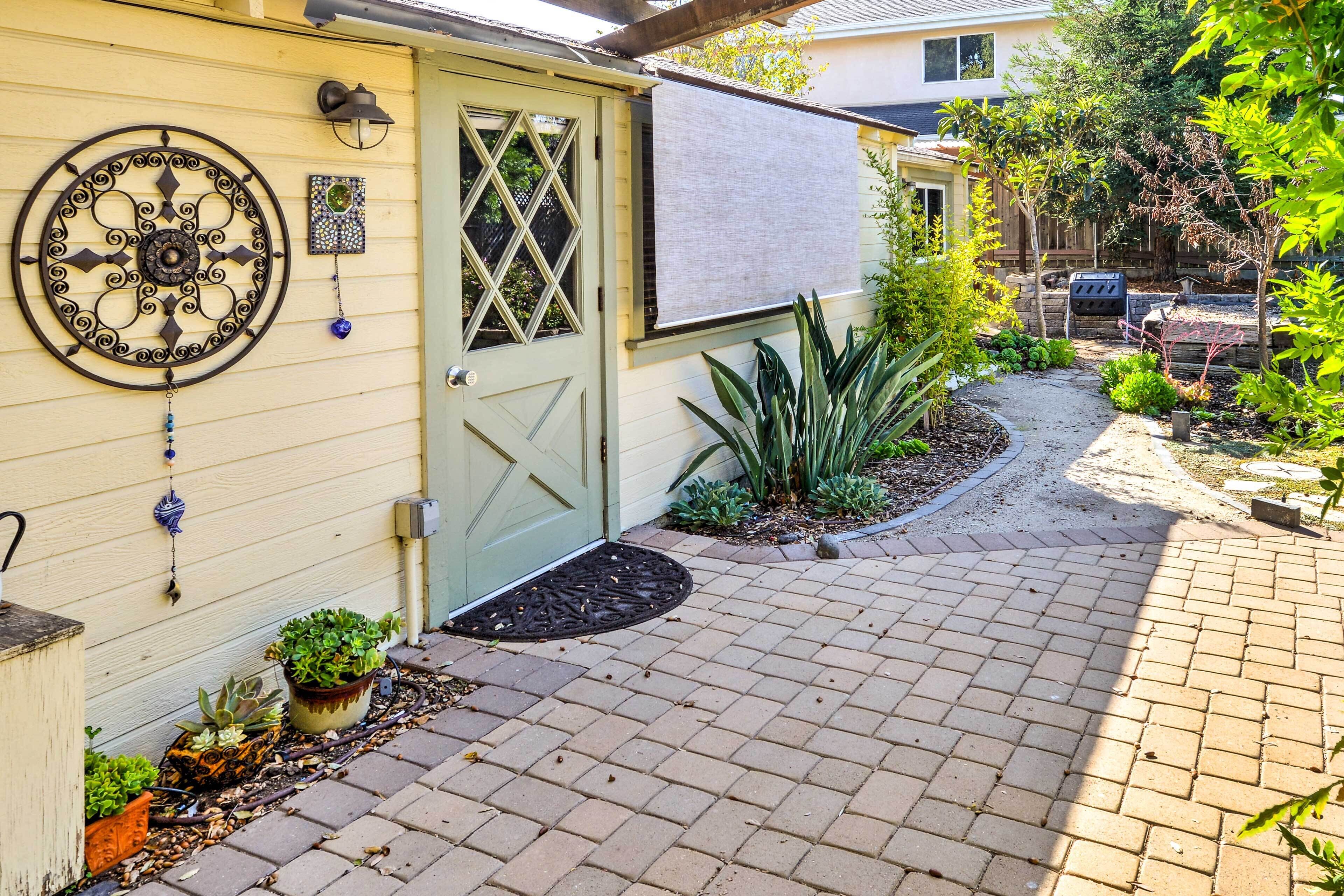 Una casa con puerta verde, un adorno metálico circular y un jardín con plantas y un sendero de ladrillos.
