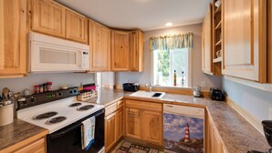 Une cuisine avec des meubles de rangement en bois, un four à micro-ondes, une cuisinière, un évier et un lave-vaisselle.