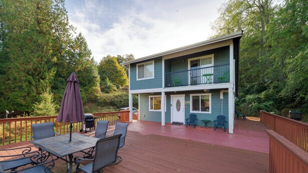 Une maison à deux étages dotée d’une terrasse, de mobilier d’extérieur et d’un barbecue.