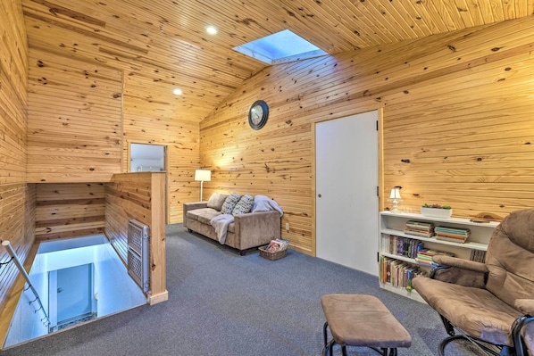 A cozy room with wooden walls, a sofa, a chair, a bookshelf, and a skylight.