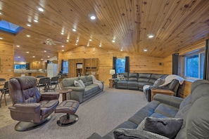 A cozy cabin interior with wooden walls, a large L-shaped sofa, a recliner, and a dining area.