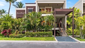 Un hotel moderno con un área exterior cubierta, palmeras y una escalera que lleva a la entrada.