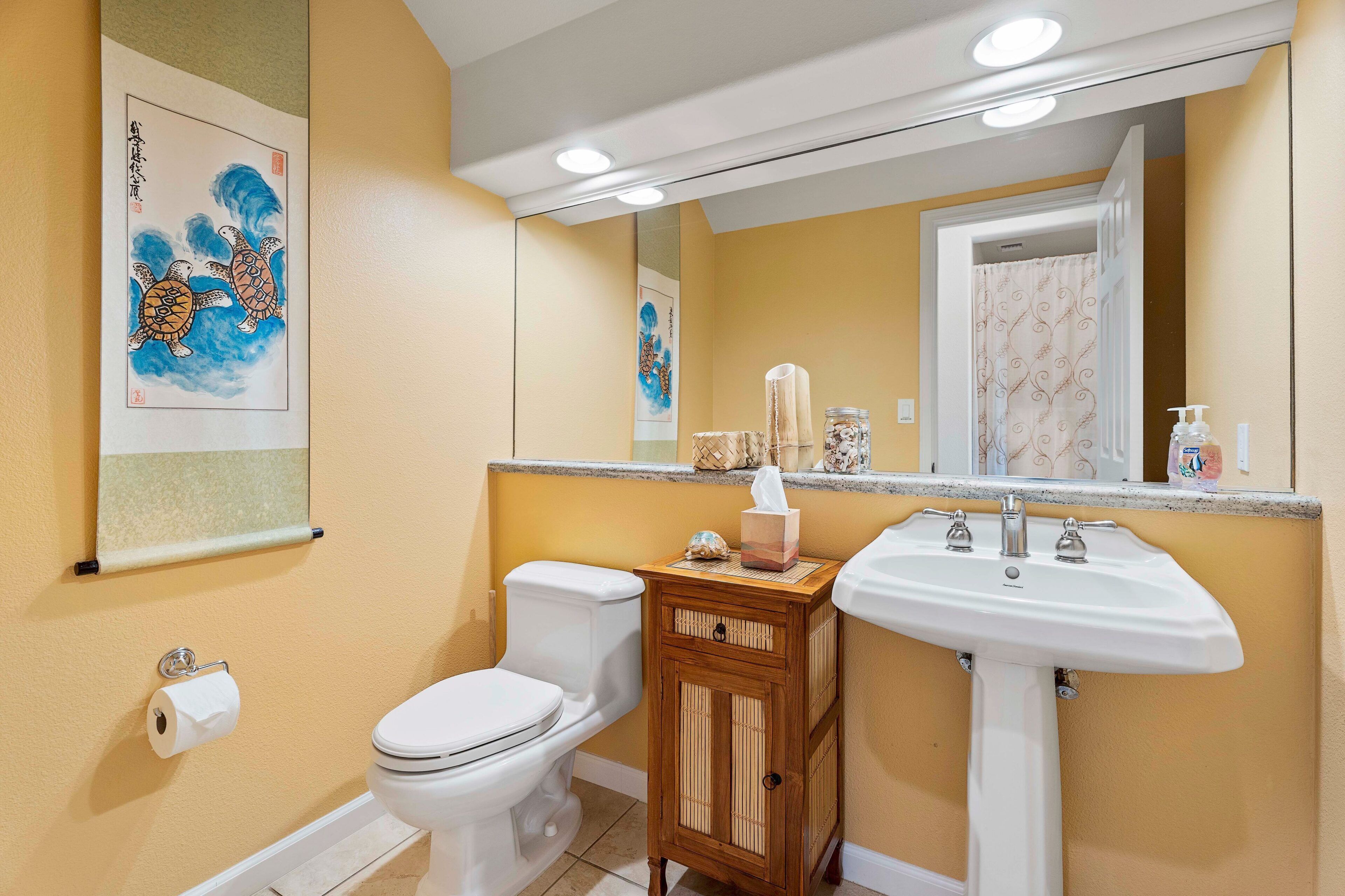 A bathroom with a toilet, sink, wooden cabinet, and a mirror.