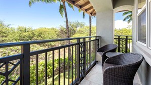 A balcony with wicker chairs, a view of palm trees, and a clear sky.