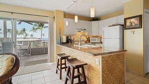Una cocina con una isla grande, armarios blancos y vistas a palmeras.