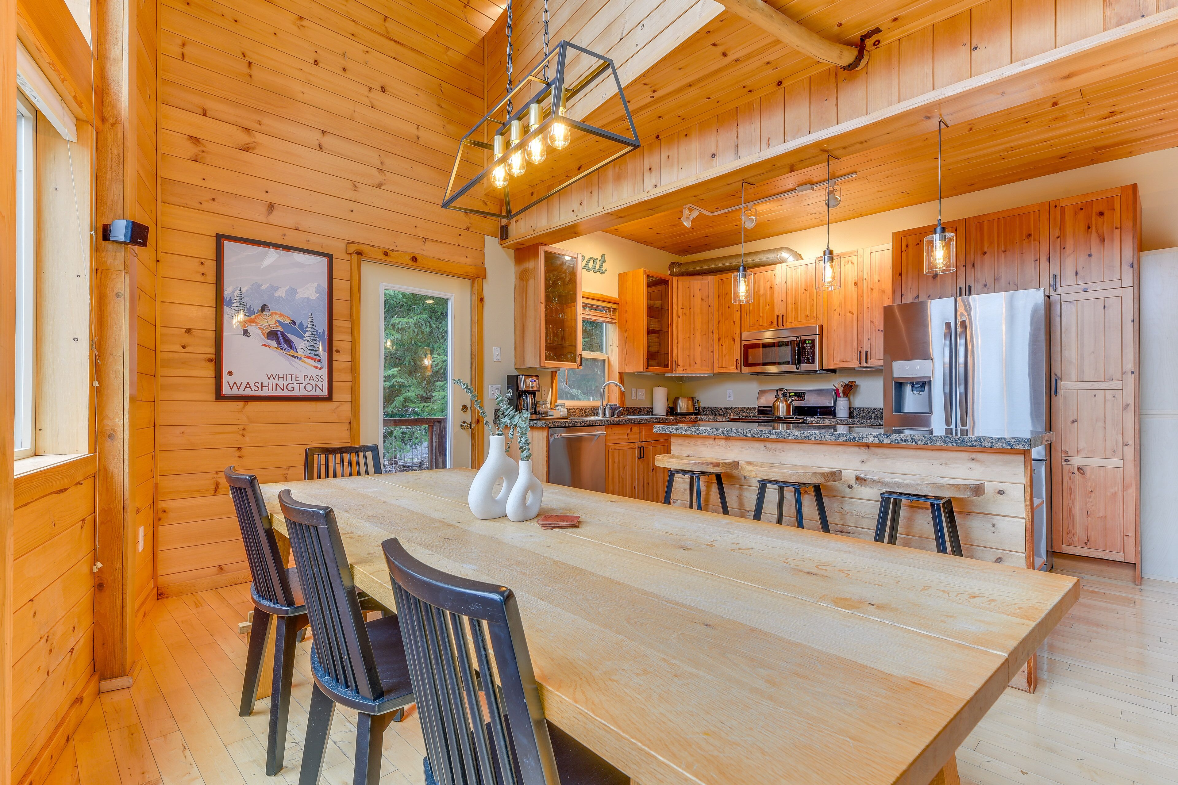 Ein Holzinterieur mit einem großen Esstisch, Stühlen, einer Küche mit Holzausbau und einer hängenden Leuchte.