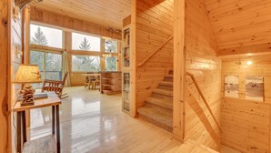Interno di una baita in legno con una scala, pavimento in legno, un tavolo con una lampada e una libreria.