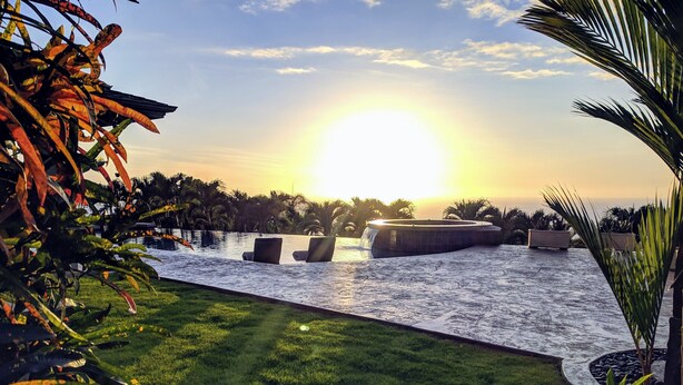 Ein Poolbereich mit Sonnenuntergangsblick, umgeben von tropischen Pflanzen und Palmen.