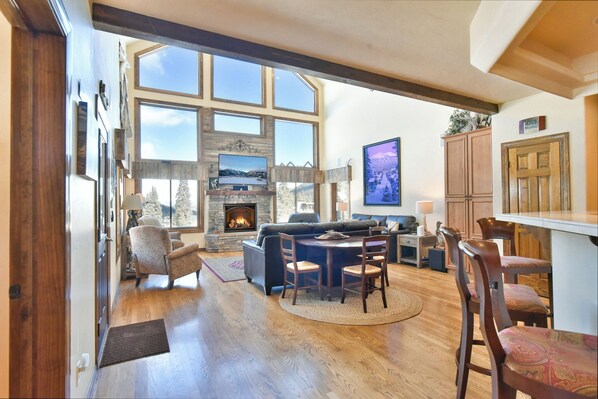 A spacious living room with a fireplace, large windows, and a stone wall.