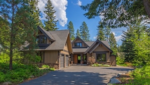 A two-story house with a stone foundation, a front porch, and a driveway leading to the garage. - Luxurious Buttercup Manor in Suncadia! Game Room | Hot Tub | Pet Friendly (Cle Elum)