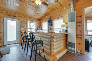 A cabin interior with a bar area, wooden walls, and a ceiling fan.