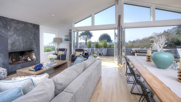 A modern living room with a fireplace, large windows, and a view of the outdoors. - Elegant Gated Beach Compound (Stinson Beach)