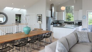 A modern kitchen with white cabinets, a central island, and a dining area with a wooden table and chairs. - Elegant Gated Beach Compound (Stinson Beach)