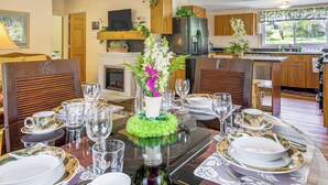 Tavola imbandita con stoviglie a tema tropicale, un centrotavola con fiori e una cucina moderna sullo sfondo.