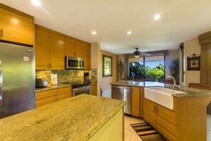 Een moderne keuken met granieten werkbladen, roestvrijstalen apparatuur, houten keukenkastjes en een groot schiereiland met een spoelbak.