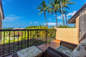 A balcony with wicker furniture, a view of palm trees, and a tiled floor.