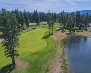 Ein Golfplatz mit Teich, umgeben von Bäumen und Häusern.