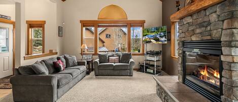 A cozy living room with a fireplace, two sofas, a coffee table, and a TV mounted on the wall.