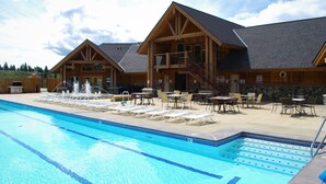 Un espace piscine avec des chaises longues et un bâtiment à l’extérieur en bois et aux fondations en pierre.