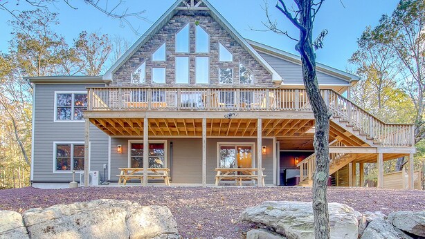 A two-story log cabin with a balcony, stone exterior, and a stone fireplace.