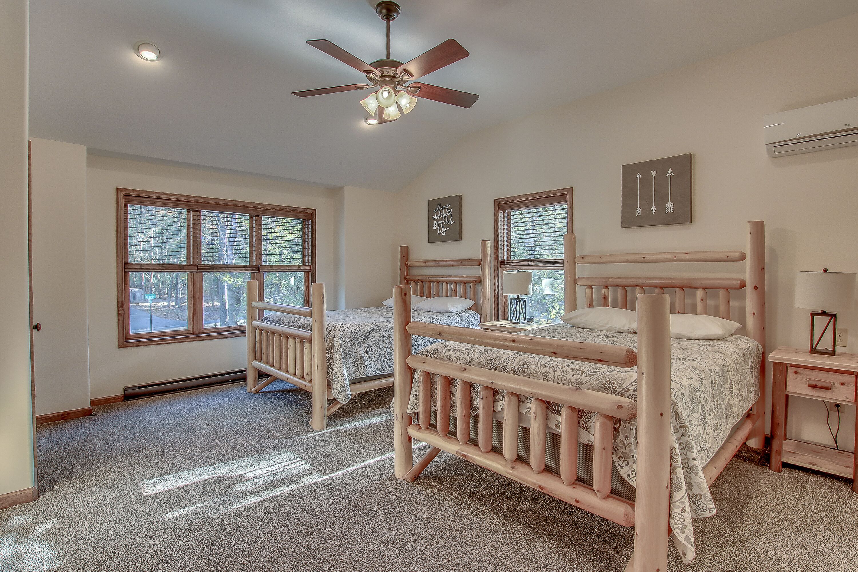 A bedroom with two wooden beds, a ceiling fan, large windows, and a carpeted floor.