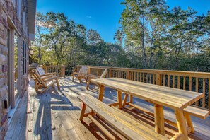 A wooden deck with picnic tables and chairs, surrounded by trees. - Summit by PMR, 8BR Guest Favorite, Elevator, Handicap Accessible, Sleeps 26 (Lake Harmony)