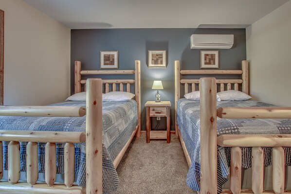 Una habitación con dos camas de madera, una mesita de noche con lámpara y un equipo de aire acondicionado en la pared.