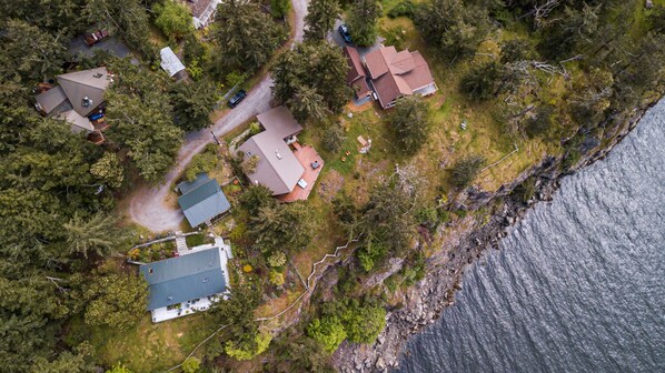 Vista aérea de uma área residencial costeira, com casas, uma estrada e um corpo de água.