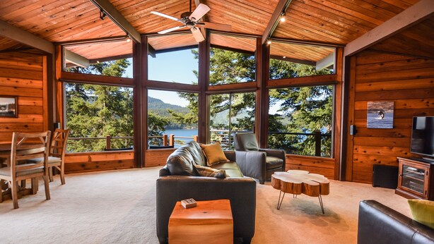 Ein geräumiges Wohnzimmer mit großem Fenster mit Seeblick, einem Deckenventilator und einer gemütlichen Sitzecke mit Sofa und Sesseln.