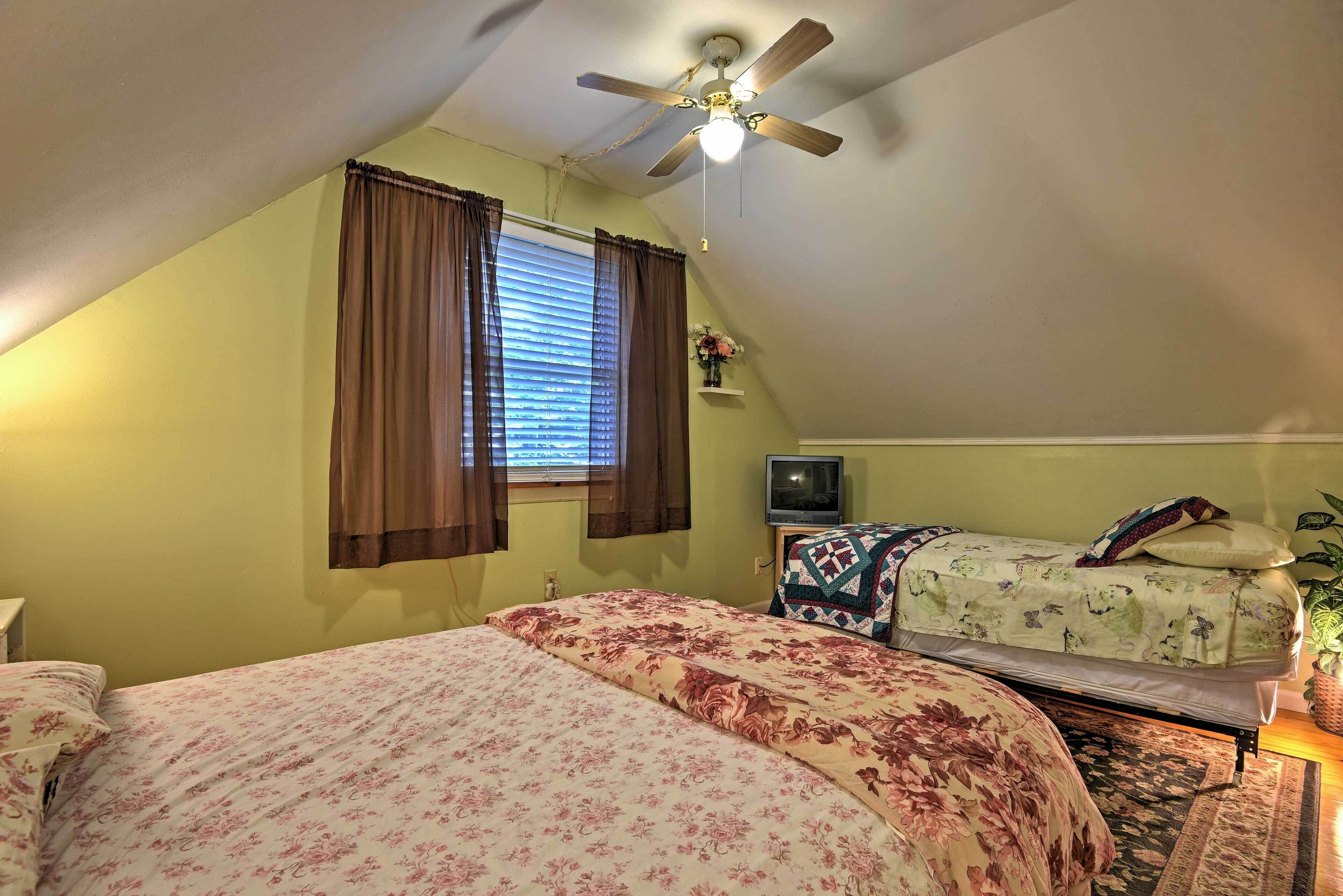 A bedroom with two beds, a ceiling fan, a TV, and a window with curtains.