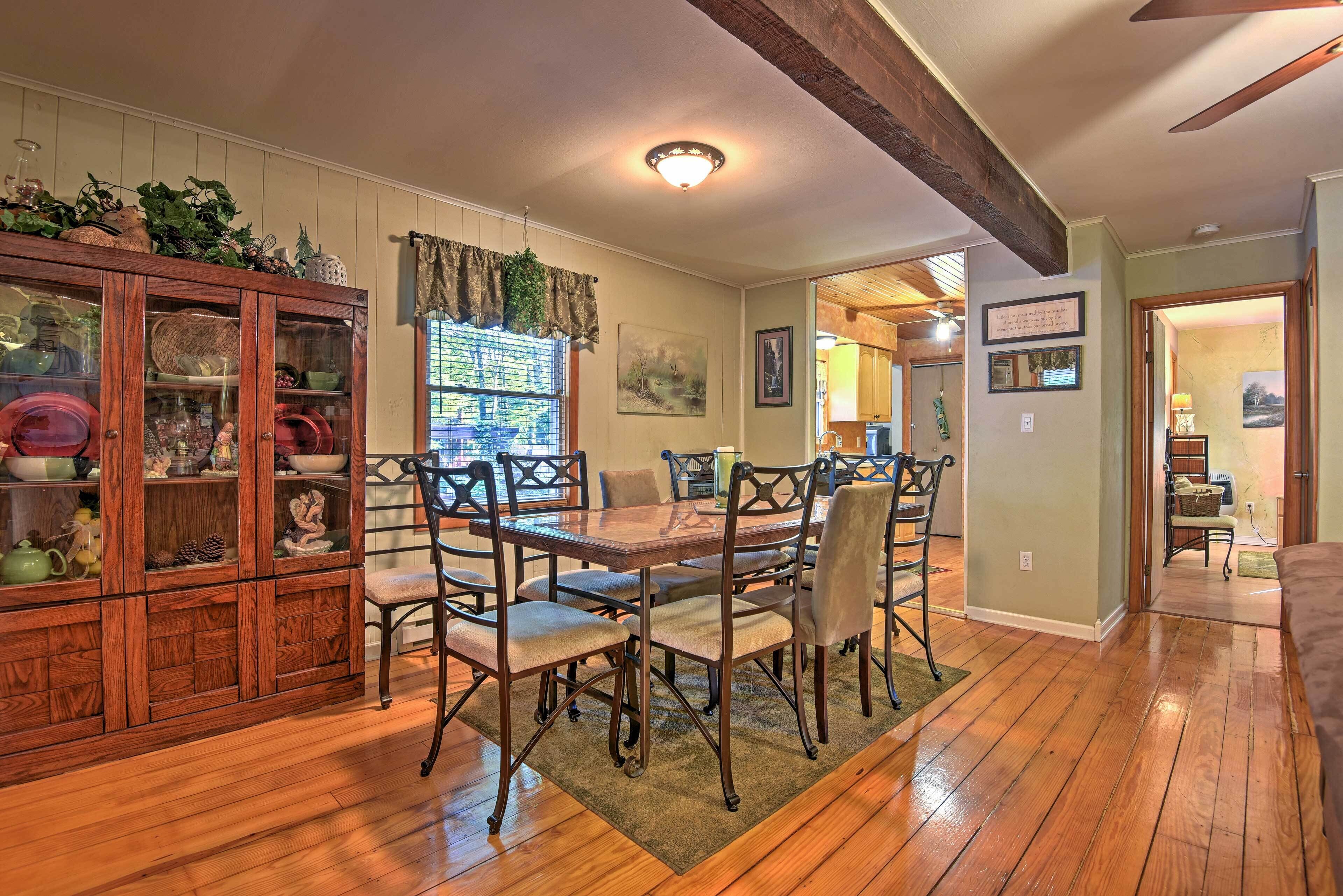 A dining room with a wooden table and chairs, a cabinet with glass doors, and a ceiling fan.