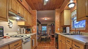 A kitchen with wooden cabinets, a stove, and a dining area with a table and chairs. - 1 Mi to Lake Wallenpaupack: Pocono Mountain Home! (Greentown)