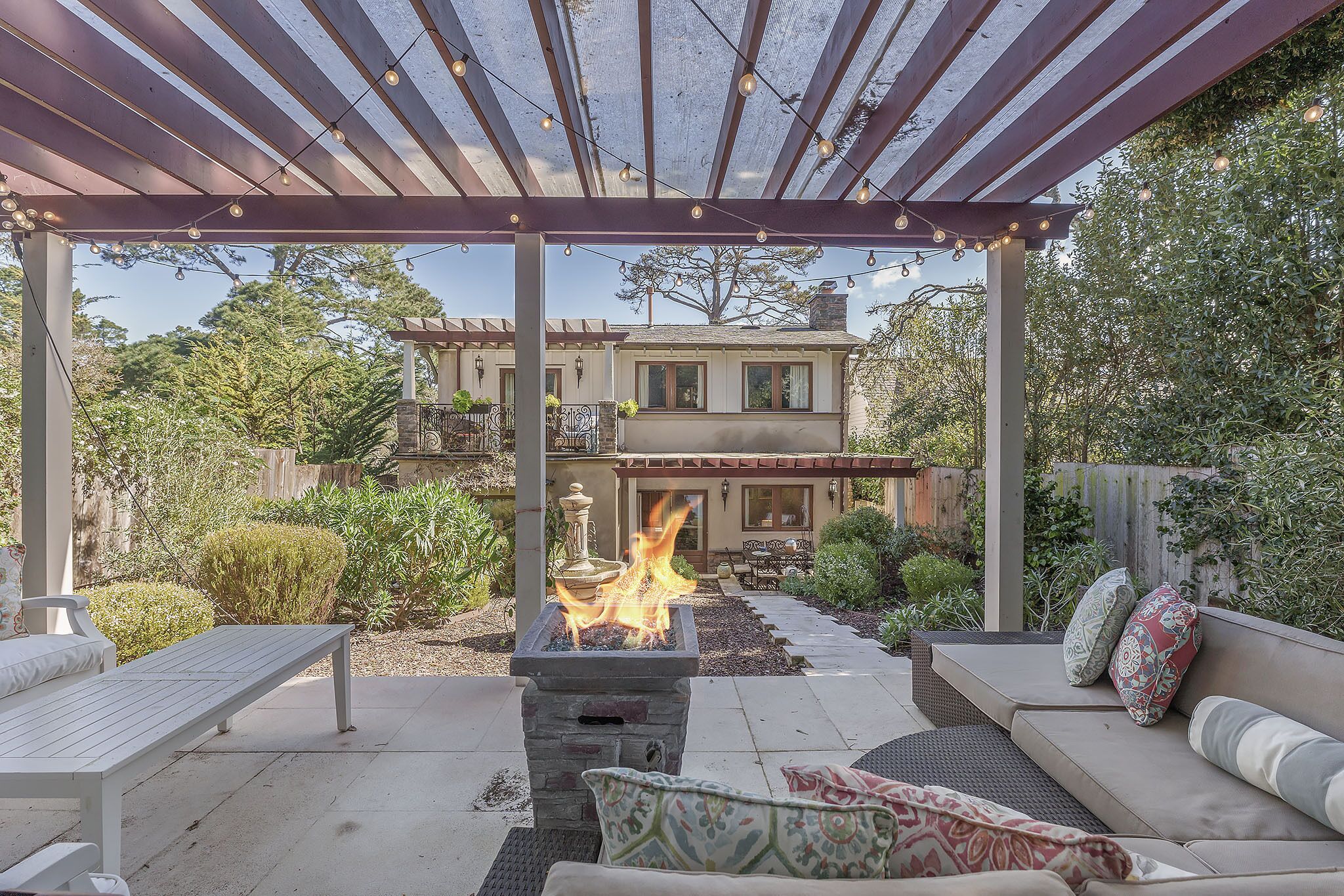 A covered patio with a fire feature, outdoor seating, and a view of a house.