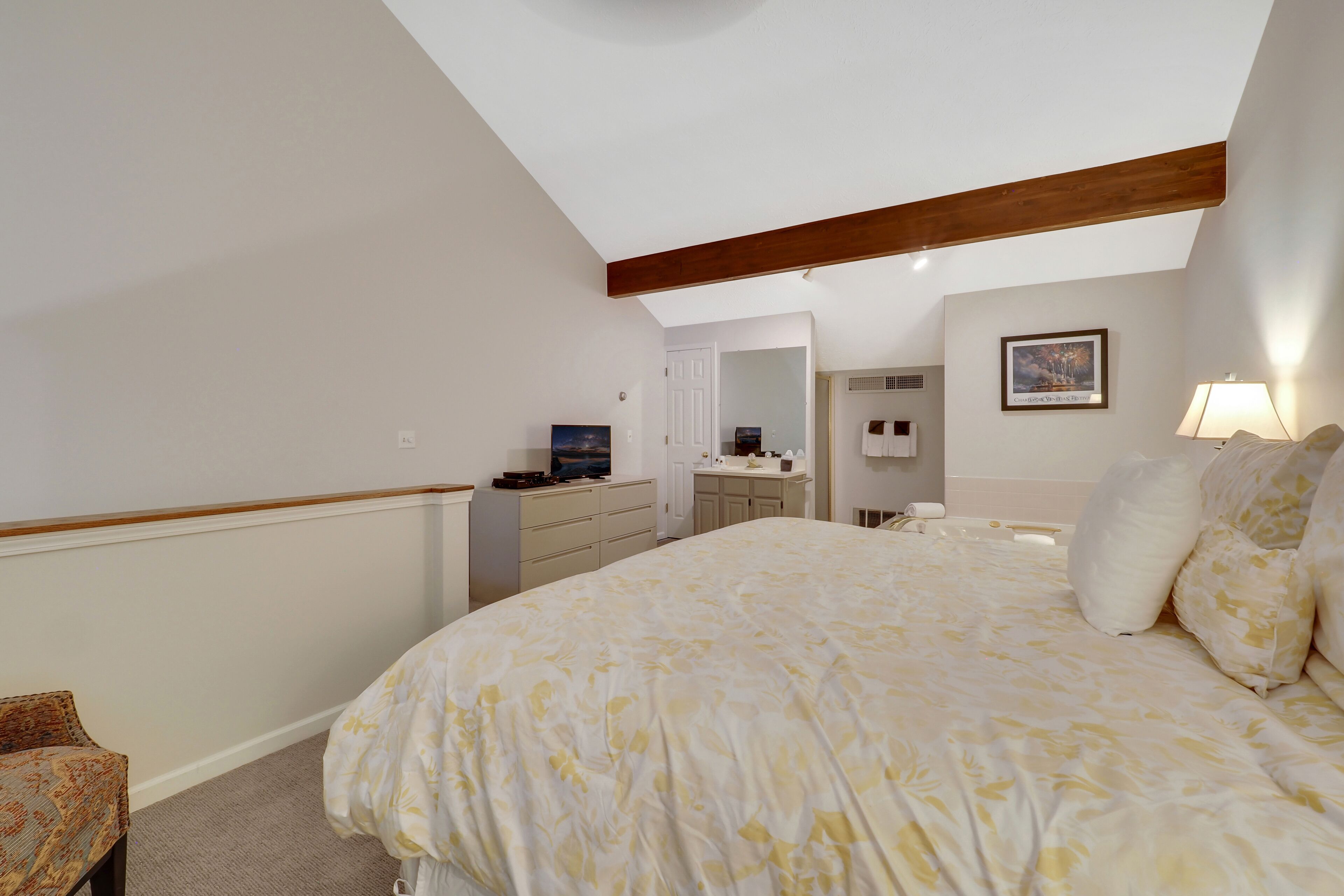 A bedroom with a large bed, a desk, a chair, a dresser, a mirror, and a window.