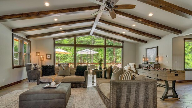 A spacious living room with a high ceiling, large windows, a sofa, a coffee table, and a foosball table. - In the Wild Woods - TLUXP (Tahoe Vista)